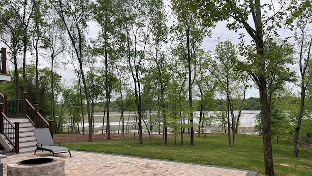 A patio with a stone fire pit and a chair, overlooking a lake with trees. - SPACIOUS Single Home near DC & National Harbor (Fort Washington)
