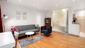 A modern living room with a grey sofa, a small round table, a dark armchair, and a wooden floor. - Apartment 'Grüne Oase In Der Großstadt' with Private Terrace, Garden and Wi-Fi (Berlin)