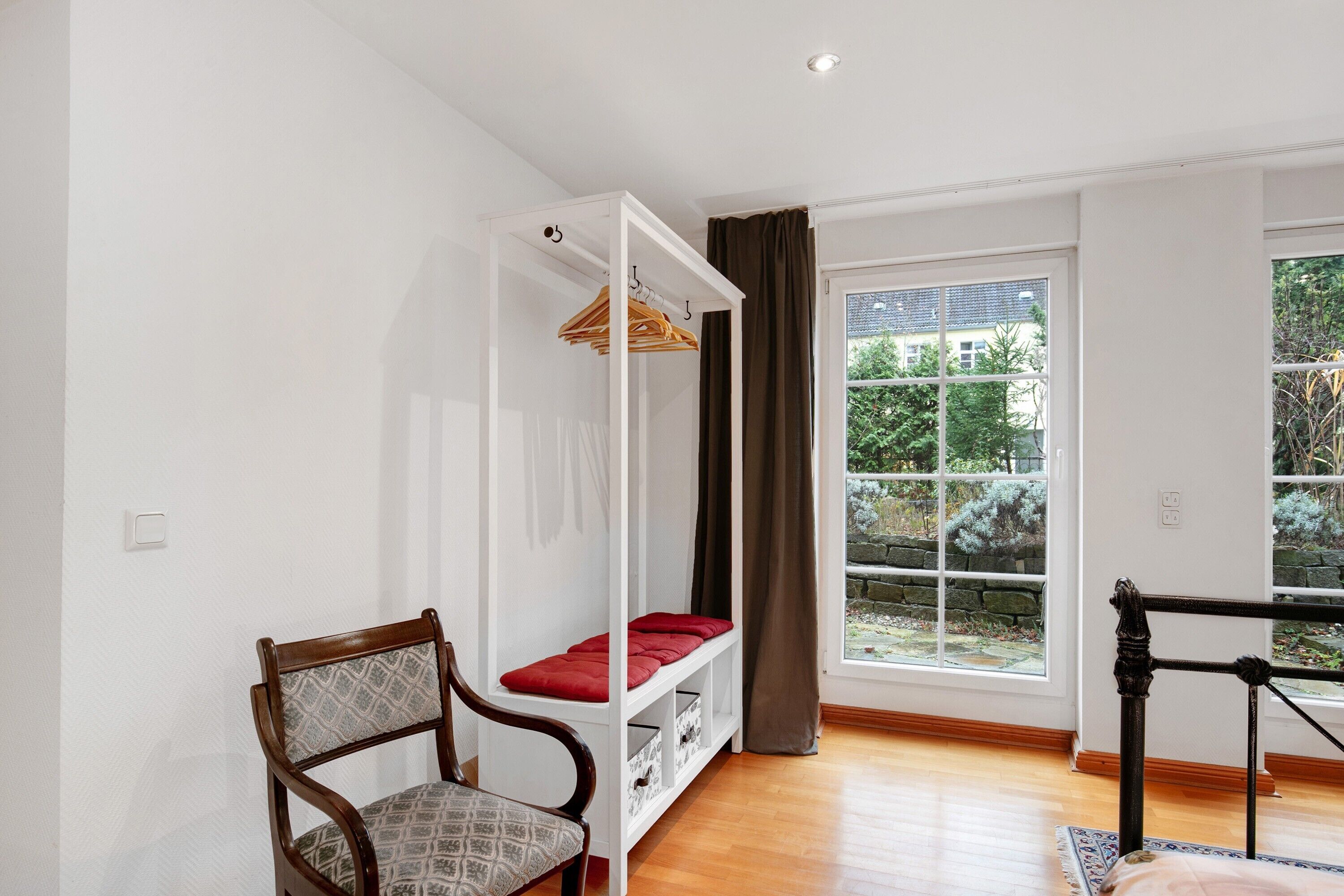 A room with a bed, a chair, a wardrobe, and a window with a view of greenery.