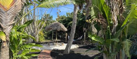A garden with a thatched-roof structure, a brick pathway, and various tropical plants.