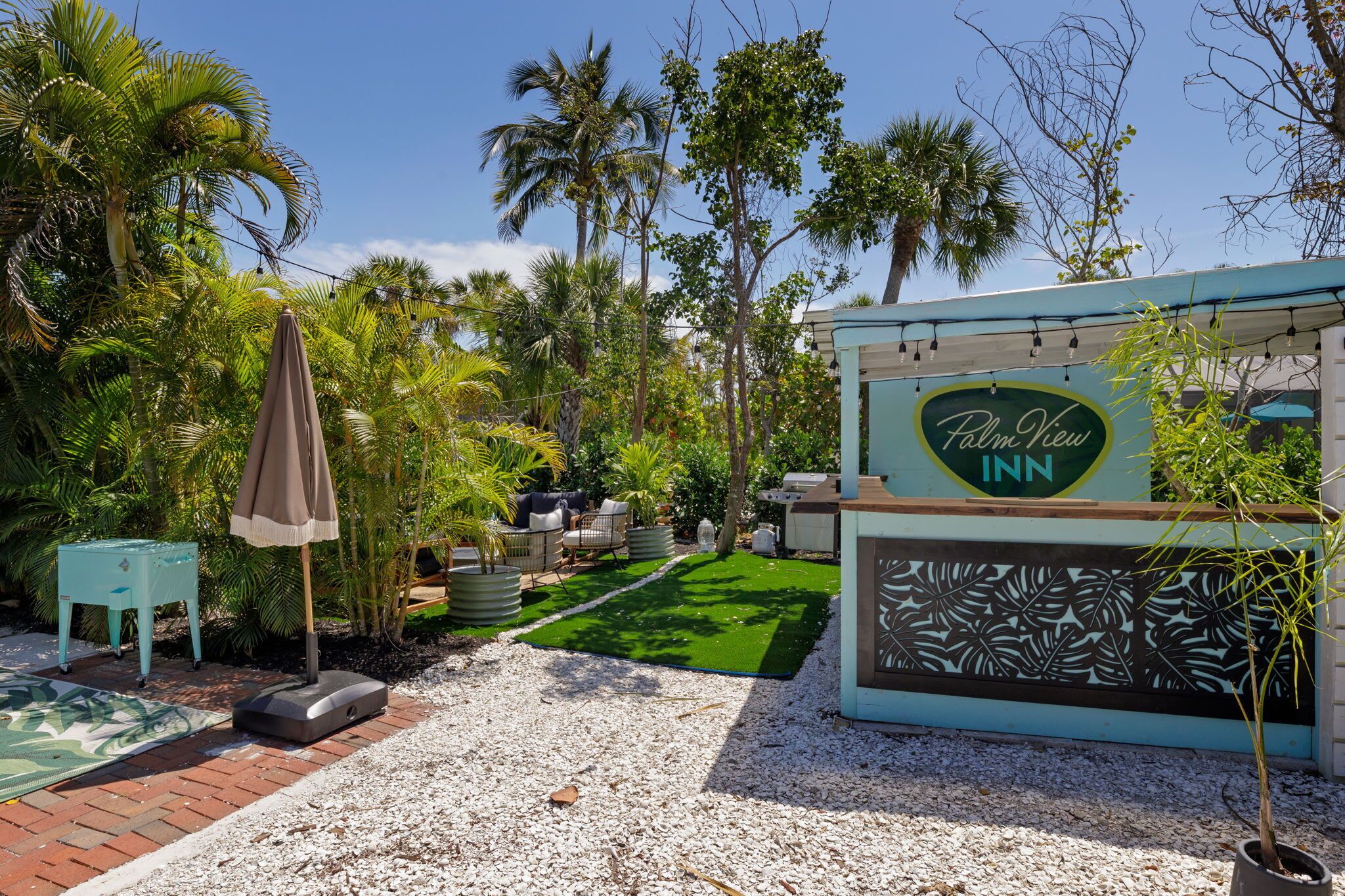 Une enseigne de l’hôtel Palm View, avec un jardin tropical et un espace extérieur aménagé pour s’asseoir.