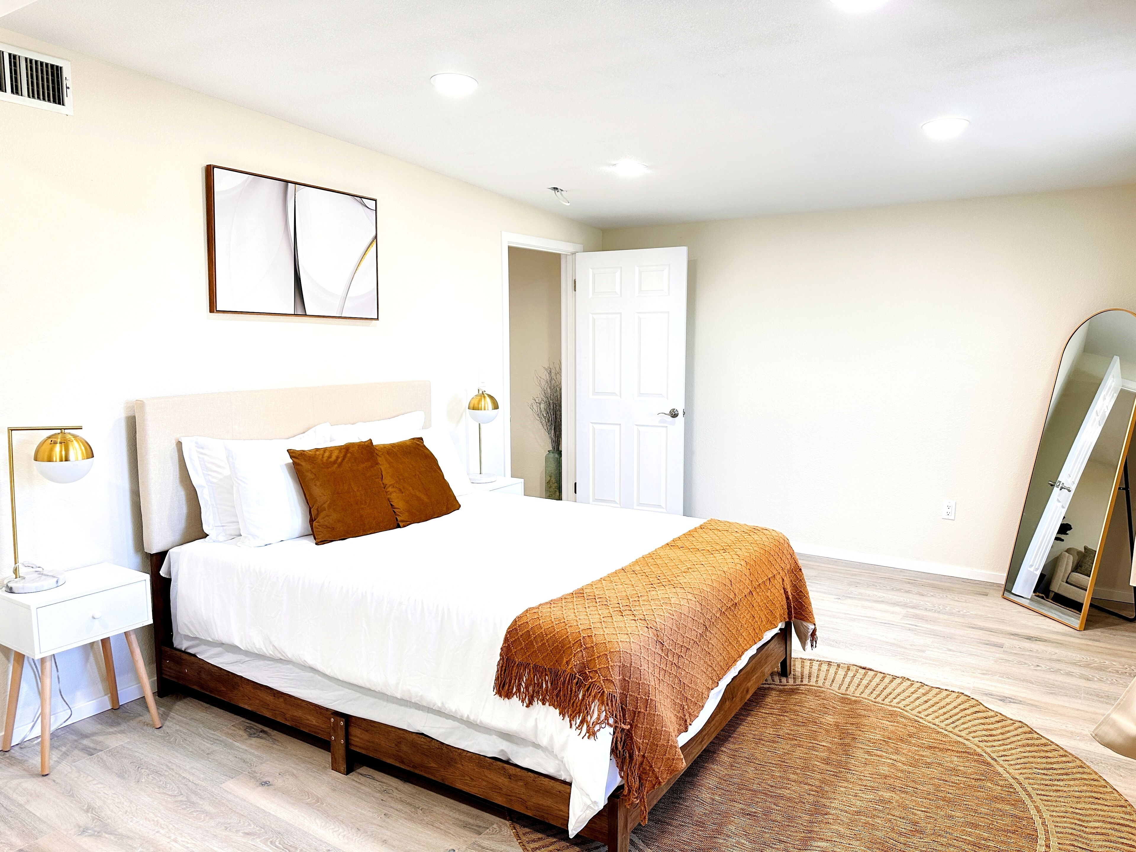 A bedroom with a bed, bedside tables, a lamp, a mirror, and a door.
