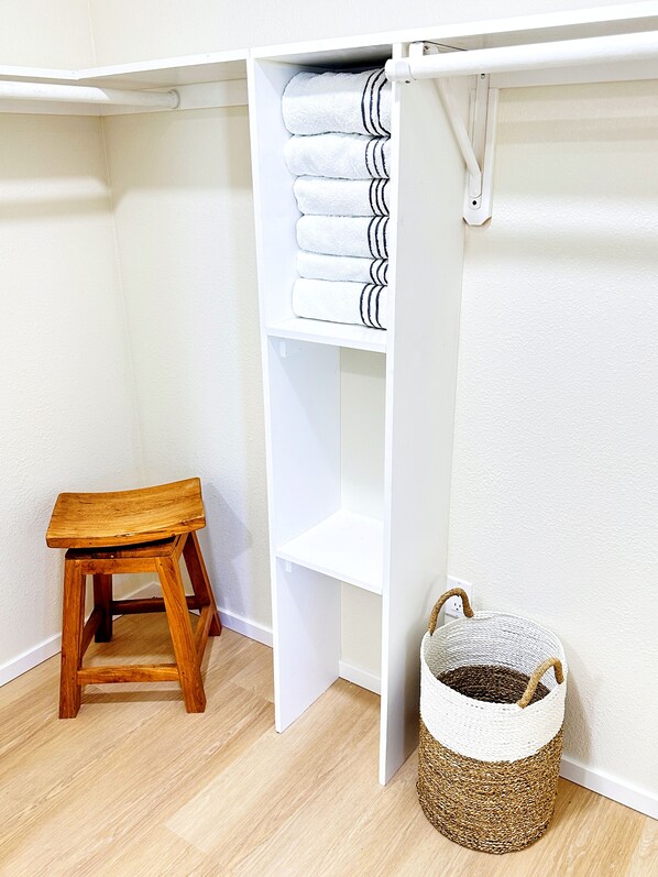 Un placard blanc avec des étagères, un tabouret en bois et un panier en osier.