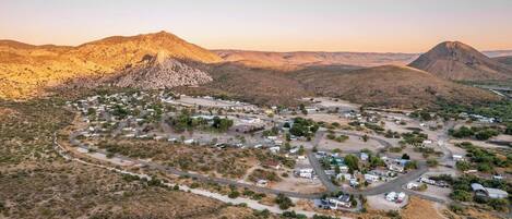 An aerial view of a desert town with winding roads and sparse vegetation, surrounded by mountains.