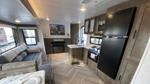 Cucina compatta per camper, con piano cottura integrato, frigorifero e zona salotto.