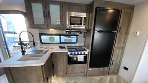Una cucina compatta con forno a microonde, fornello e frigorifero.