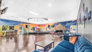 Eine geräumige Lobby mit einem blauen Sofa, einem Klavier und einer Bühne mit Wandgemälde.