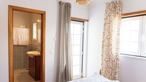 Ein Schlafzimmer mit Bett, Fenster, Tür und einem Badezimmer mit Waschbecken und Spiegel.