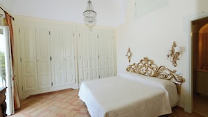A bedroom with a large bed, a chandelier, white wardrobes, and a door leading to another room. - Ancient mansion with breathtaking views amid ancient olive and citrus trees (Praiano)