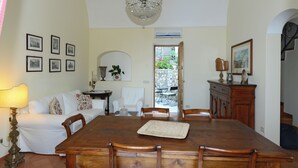 A dining room with a wooden table, chairs, a chandelier, and a white sofa. - Ancient mansion with breathtaking views amid ancient olive and citrus trees (Praiano)