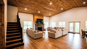 Un amplio salón con escalera de madera, dos sofás, una chimenea y un televisor montado en la pared.