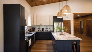 Una cocina moderna con armarios oscuros, una isla de mármol y techo de madera.