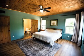 Een slaapkamer met een bed, houten plafond en een raam met gordijnen.
