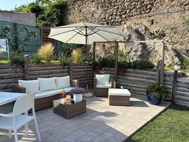 Un patio exterior con un sofá de mimbre, una mesa de comedor y un paraguas grande.