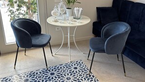 Una sala moderna con dos sillones azul oscuro, una mesa redonda blanca con adornos de vidrio, una planta en maceta y un sofá azul oscuro.