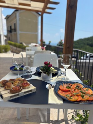 Mesa al aire libre con diversos alimentos, vasos de agua y una planta en maceta.