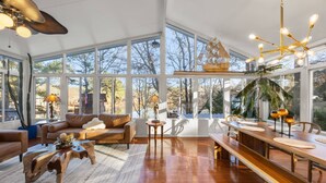 A spacious living area with a large window, a wooden dining table, and a ceiling fan. - Pool, Tree House, Kids Game Room, Grilling & 20 Minutes to Atl Attractions (Lilburn)