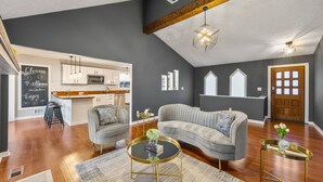 A modern living room with a grey sofa, two armchairs, a coffee table, and a kitchen in the background. - Pool, Tree House, Kids Game Room, Grilling & 20 Minutes to Atl Attractions (Lilburn)