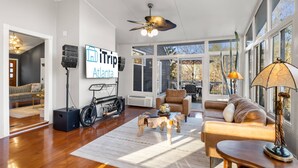A spacious living room with a large window, a ceiling fan, and a sign for 'iTrip Atlanta'. - Pool, Tree House, Kids Game Room, Grilling & 20 Minutes to Atl Attractions (Lilburn)