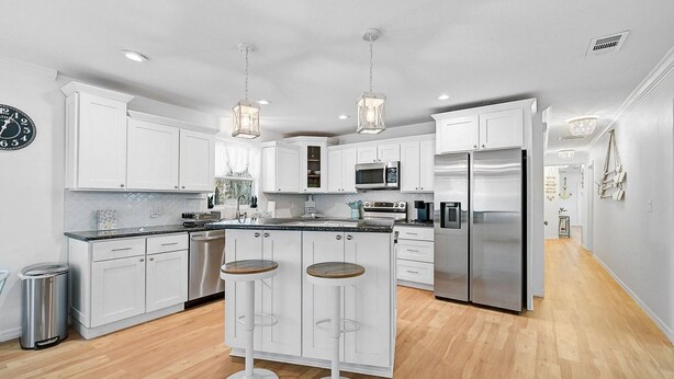 A modern kitchen with white cabinets, stainless steel appliances, and a bar stool area. - Manatee Cottage - Private Pool, Tropical Oasis! (Bradenton)