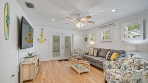 A living room with a ceiling fan, a sofa, a coffee table, and a TV. - Manatee Cottage - Private Pool, Tropical Oasis! (Bradenton)
