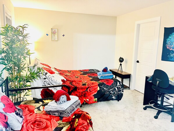 A bedroom with a bed, a desk, a chair, a potted plant, and a wall with a framed picture.