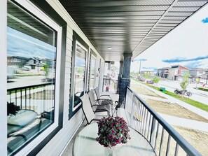 A balcony with a view of a residential street, a hanging flower arrangement, and outdoor seating.
