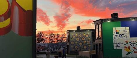 A building with a green facade and a yellow arrow sign, a paved area with a wooden bench, and a sunset sky.