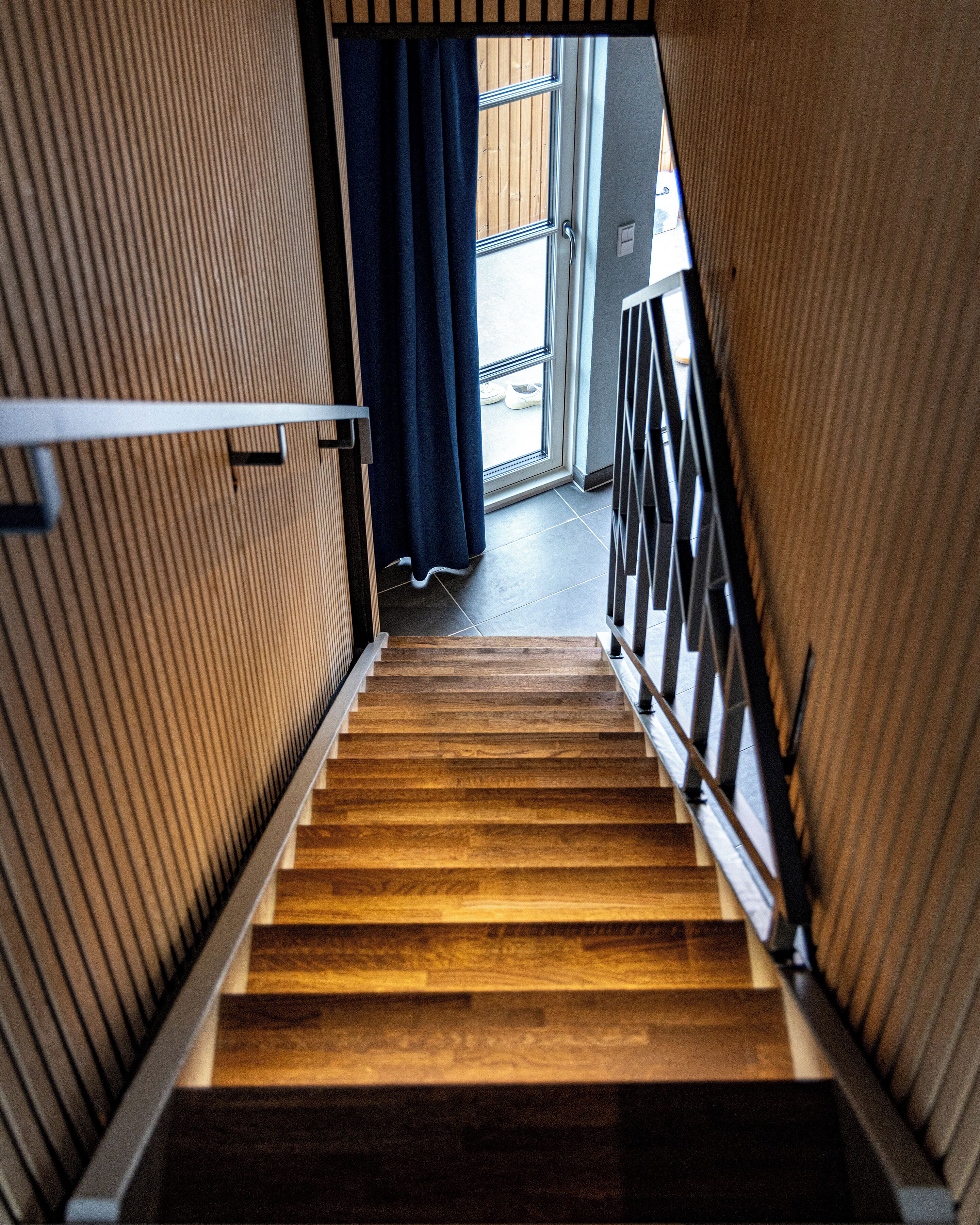 Una escalera de madera con barandillas de metal que conduce a una puerta con cortina azul.