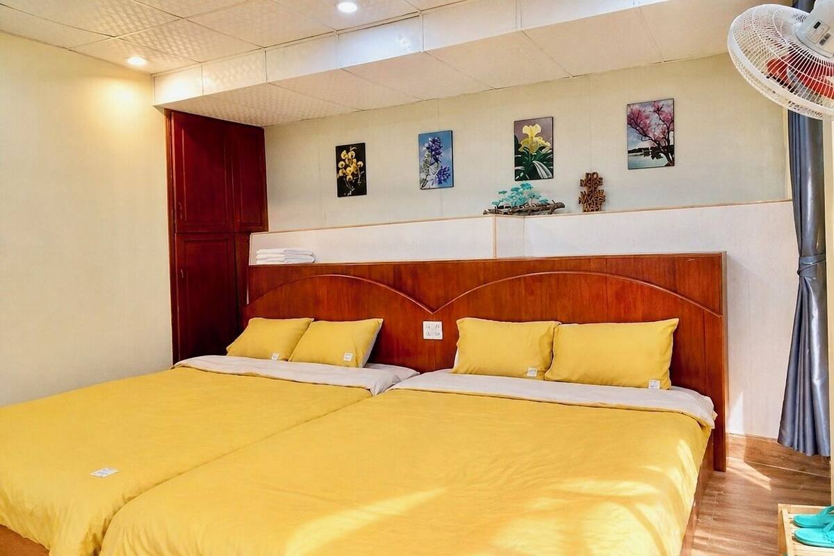 A double bed with yellow bedding, a wooden headboard, and a bedside table with a fan.