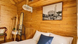 Ein Zimmer mit Holzwandverkleidung, einem Bett, einem Deckenventilator, einem Kleiderständer und einem gerahmten Bild an der Wand.