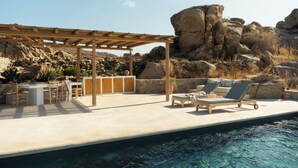 Ett område vid poolen med en pergola, solstolar och en matplats.