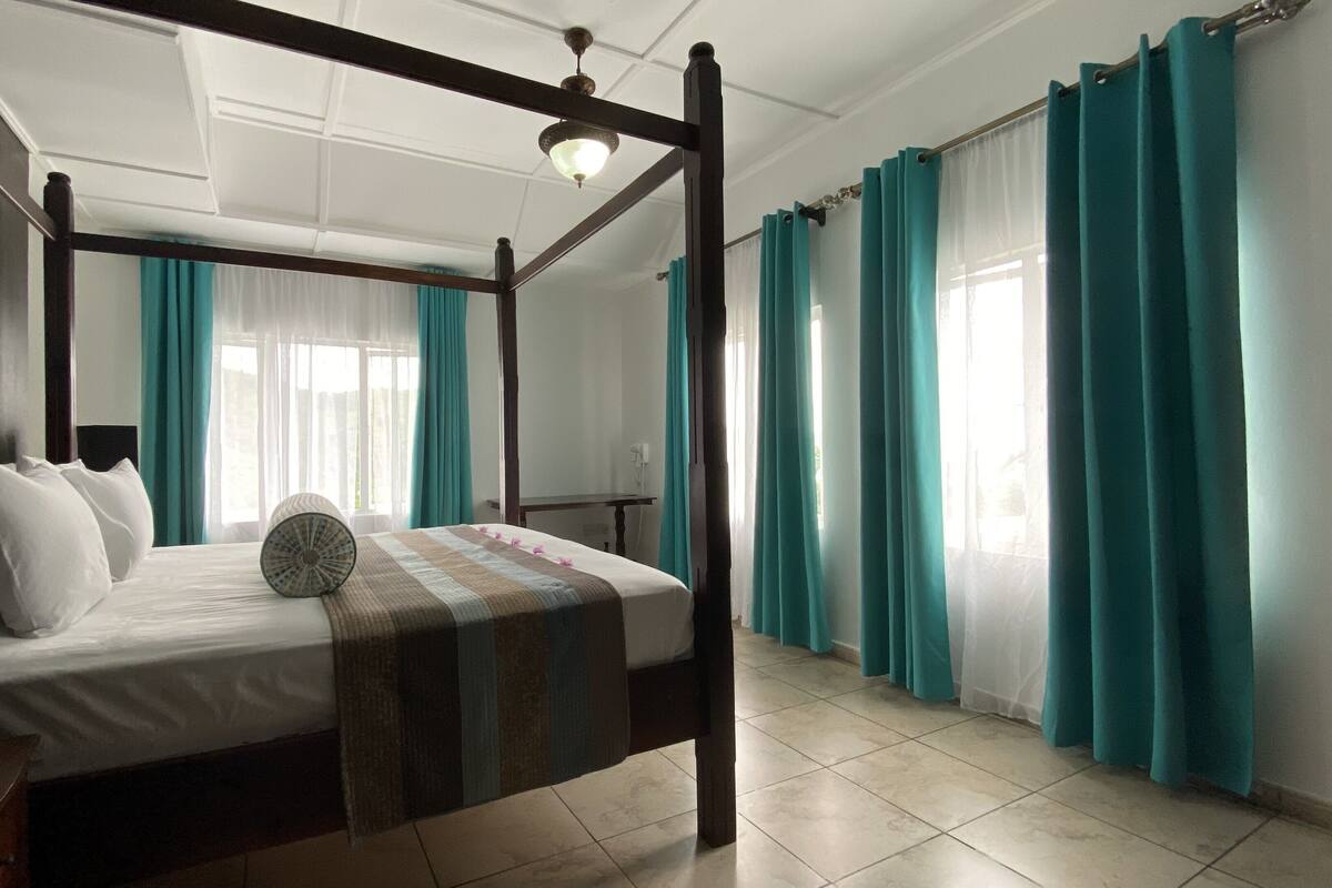 A four-poster bed with a quilt, a bedside table, and a nightstand.