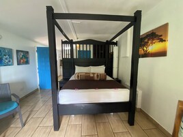 Una cama con dosel con una colcha marrón y almohadas blancas, una silla azul y un cuadro de un atardecer en la pared.