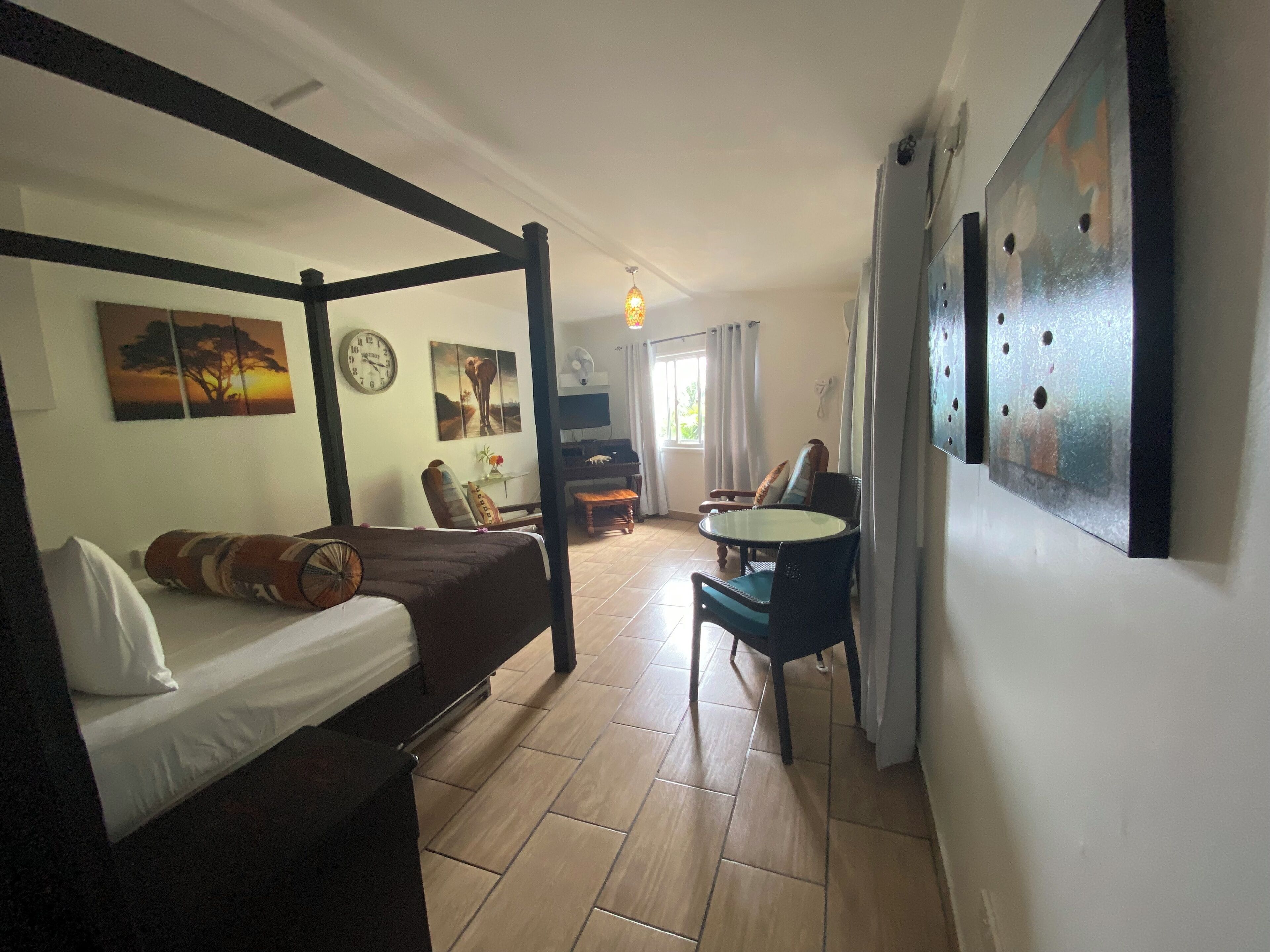 A bedroom with a four-poster bed, a desk with a chair, a TV, and artwork on the walls.