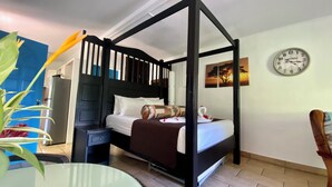 A four-poster bed with a dark headboard, a bedside table, a clock, and a wall painting.
