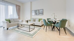 A modern living room with a sofa, coffee table, and dining area with chairs. - Luxury Stay at Madison 2bedroom Balcony (Dubai)