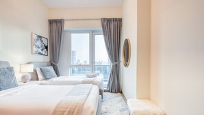 A hotel room with two beds, a large window with curtains, a city view, a round mirror, and a small round table with a lamp. - Luxury Stay at Madison 2bedroom Balcony (Dubai)