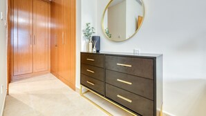 A hallway with a wooden wardrobe, a dark dresser with gold handles, and a round mirror on the wall. - Luxury Stay at Madison 2bedroom Balcony (Dubai)