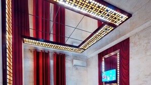 A modern hotel room with a bed, red curtains, a TV, and a patterned carpet. - Leon Hotel (Absheron)