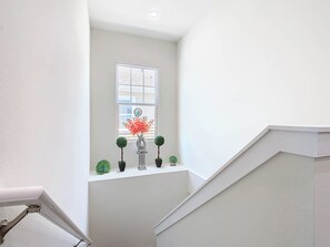Eine Treppe mit weißer Geländer, ein Fenster mit einer Uhr und ein Regal mit Blumentöpfen.