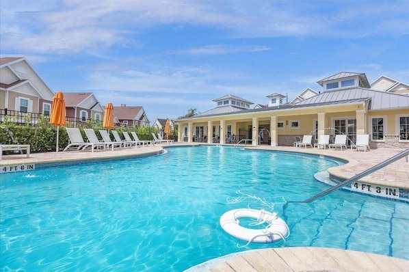 Ein Pool mit Liegestühlen und Sonnenschirmen, umgeben von Gebäuden.