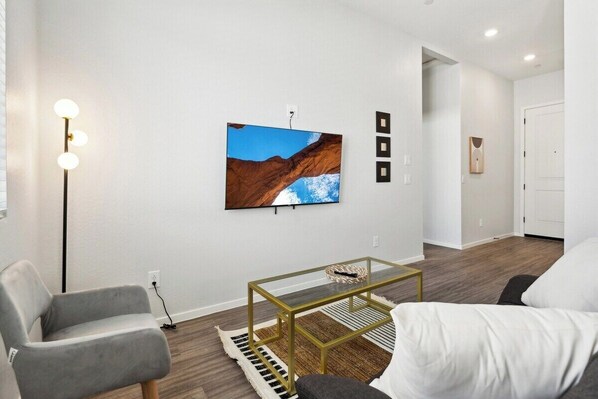 A modern living room with a mounted TV, a glass coffee table, and a grey armchair. - Sparkling Modern Home in Canopy w/ Pool,BBQ (Buckeye)