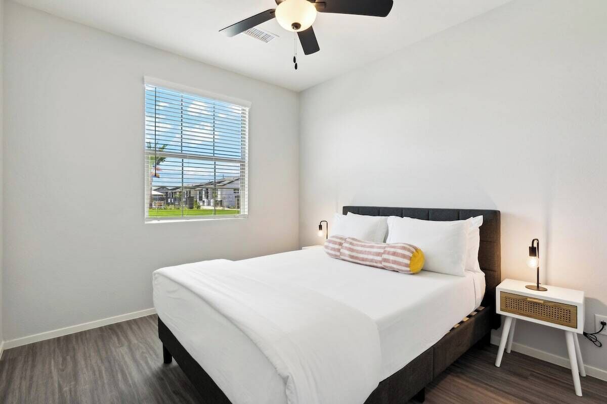 A bedroom with a bed, a nightstand, a ceiling fan, and a window with blinds.