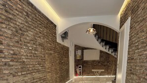 Un couloir avec un mur en briques, un escalier et un chemin éclairé.