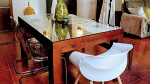 Une table à manger avec des chaises, un vase et une lampe, dans une pièce dont le sol est carrelé et qui est décorée de rideaux.