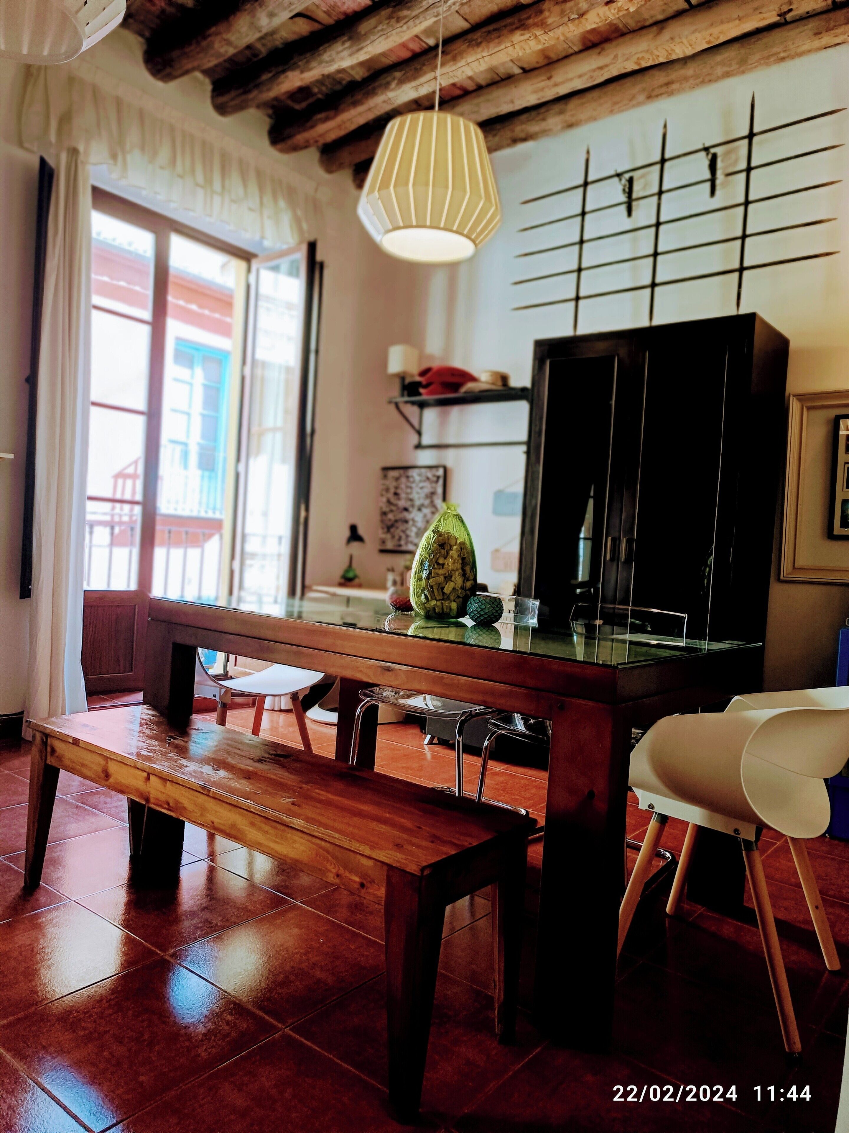 Un espacio de sala acogedor con un banco de madera, una mesa con cubierta de vidrio y una lámpara colgante.