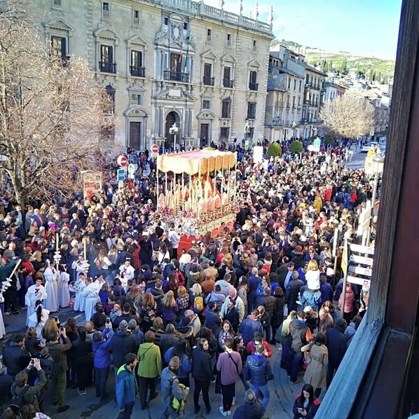 En stor menneskemængde har samlet sig omkring en central bygning, måske i forbindelse med en parade eller begivenhed, med bygninger i baggrunden.
