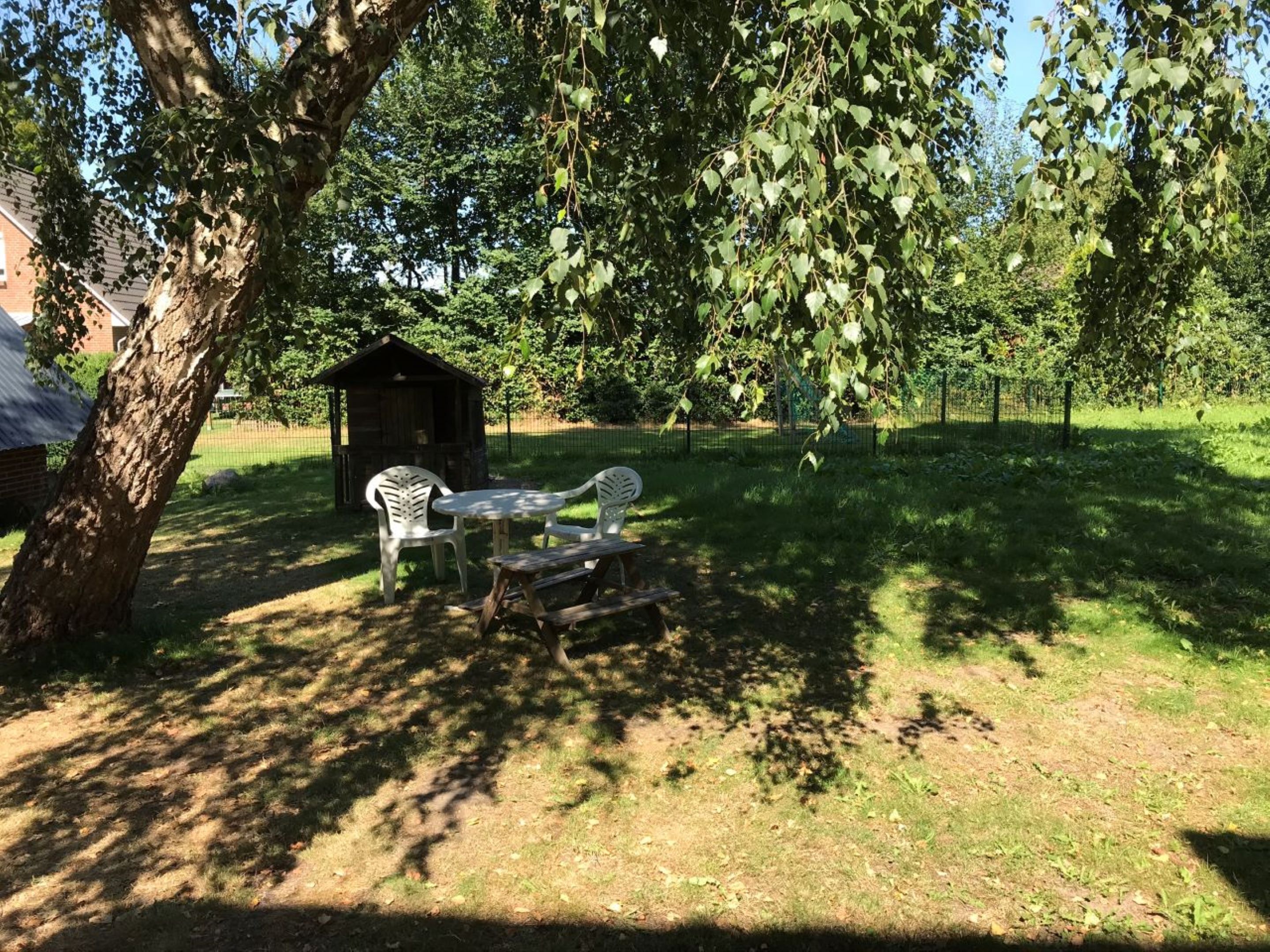 Zona de pícnic amb taula i caires, un arbre, un cobert petit i un jardí tancat.