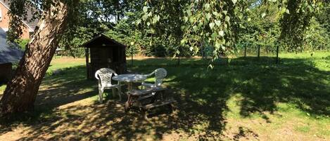 A picnic area with a table and chairs under a tree, a small shed, and a fenced garden.